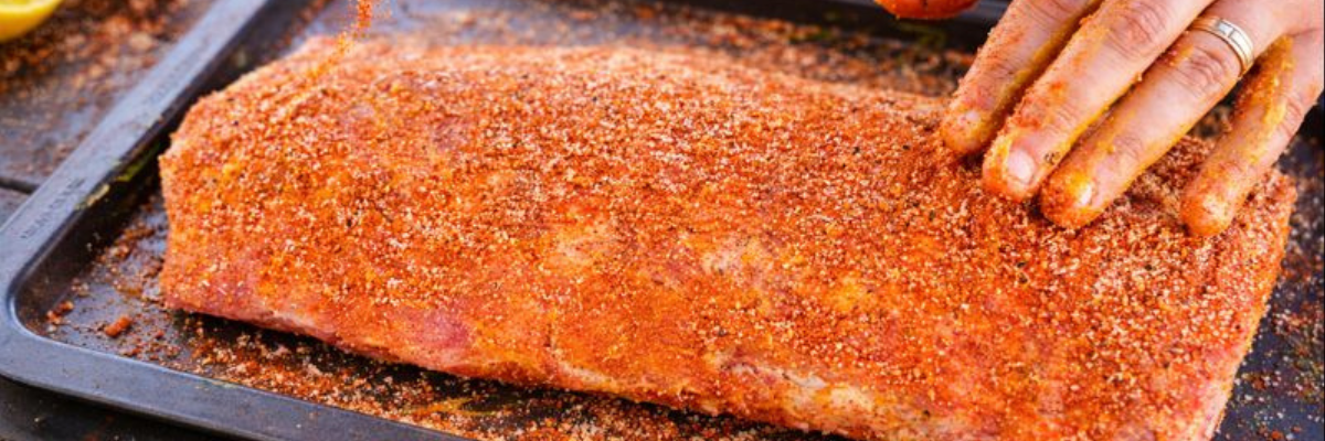 Person seasoning marinated meat before grilling.